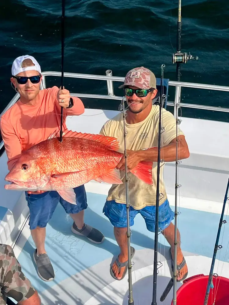Two anglers holding an oversized red snapper aboard