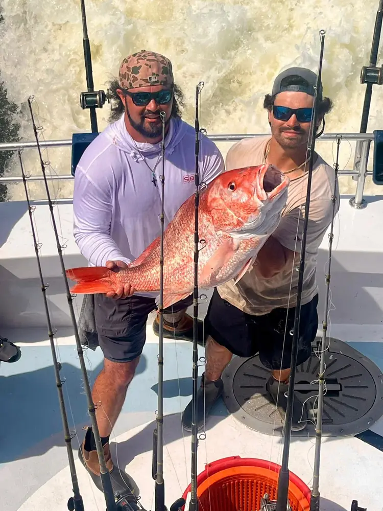 Two anglers holding heavy red snapper aboard the boat
