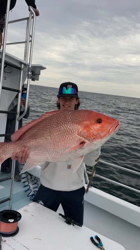 An angler holding a heavy Gulf red snapper on the back deck