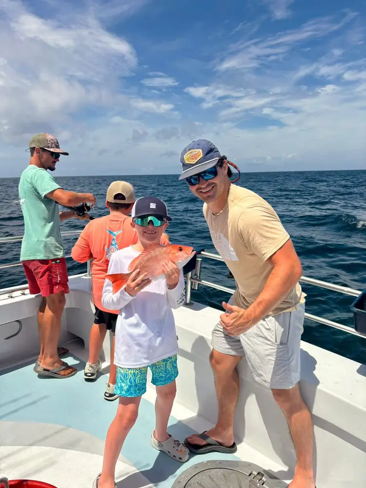 A father and son holding a red snapper aboard the boat