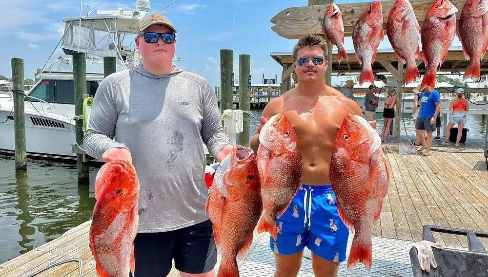 Two anglers holding red snapper at the dock