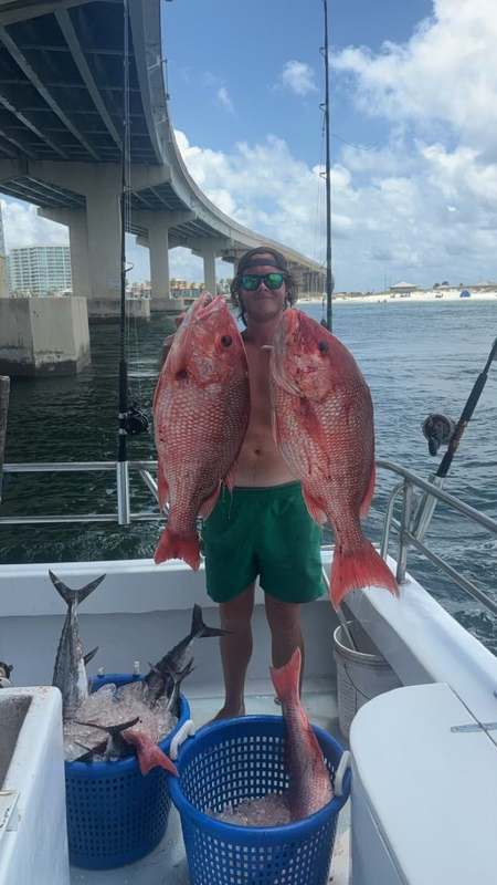 An angler holding up a big red snapper with Perdido Pass bridge behind