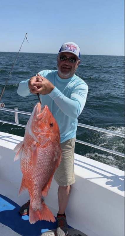 An angler holding a red snapper on the bow of the Rip Tide