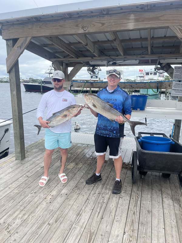 Two guests holding an amberjack on the dock in Orange Beach