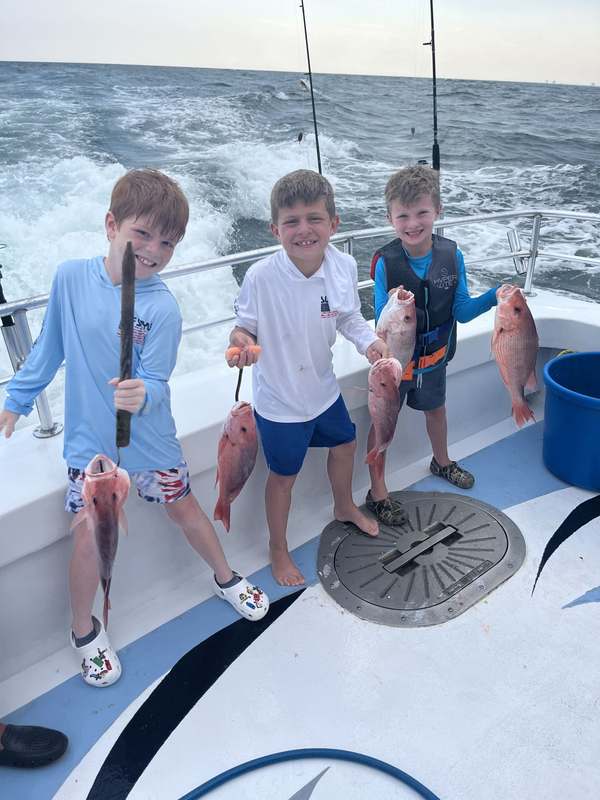 Three young anglers showing off their snapper on the back deck