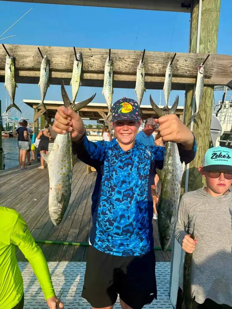 A young angler holding a pair of king mackerel at the marina