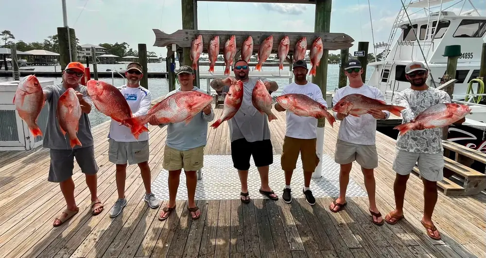 A line of anglers each holding a red snapper at the fish rack