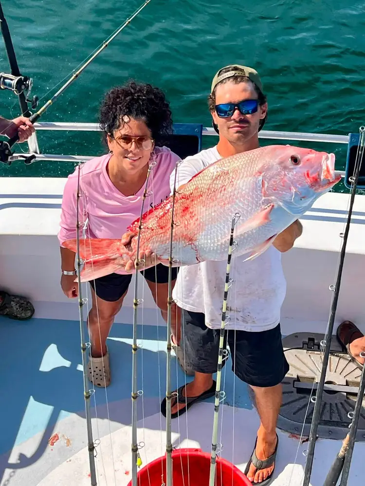 Two guests holding a bright red snapper aboard the boat
