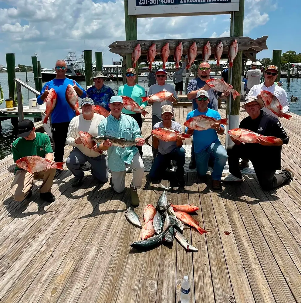 A large group with red snapper hanging behind them at the marina