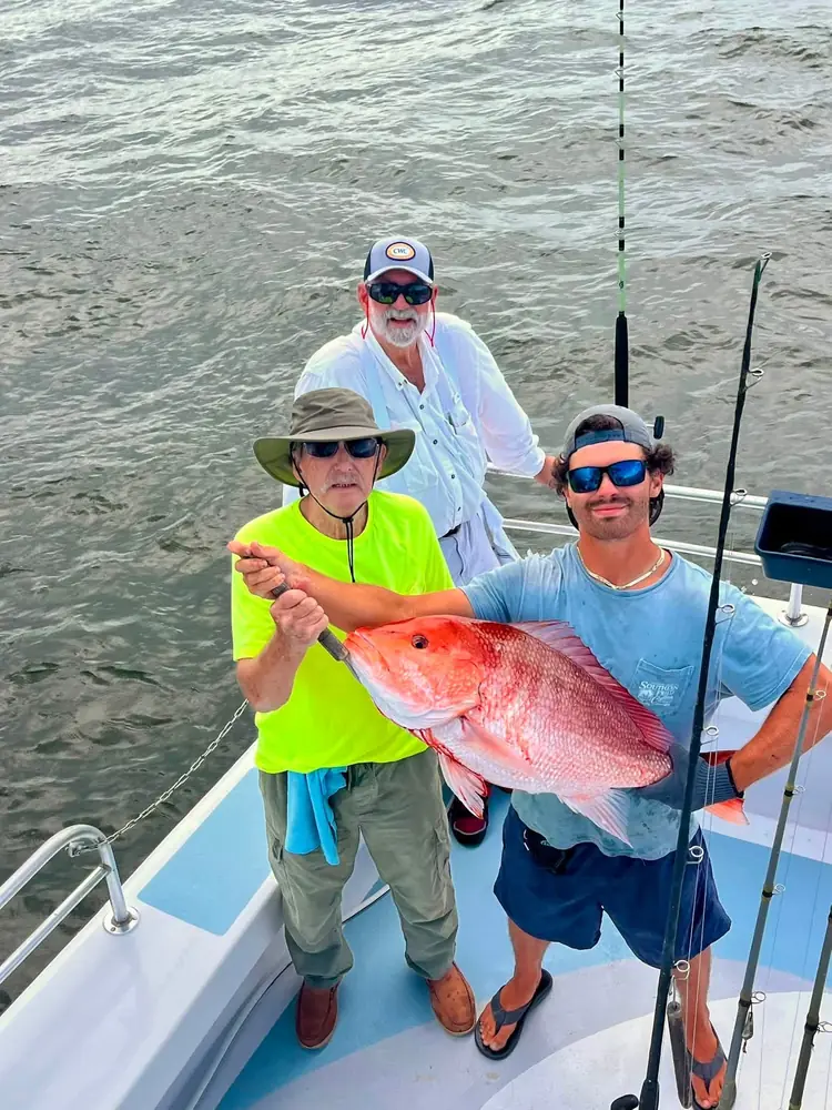 A guest and deckhand holding a red snapper aboard