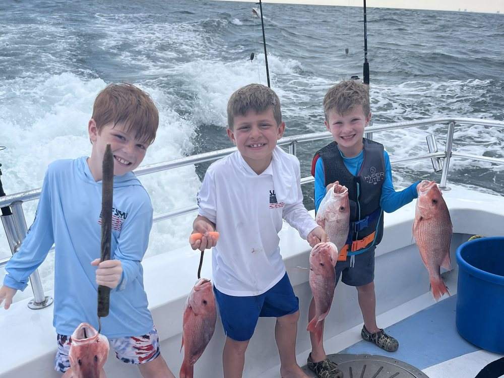 Three young anglers showing off their snapper on the back deck